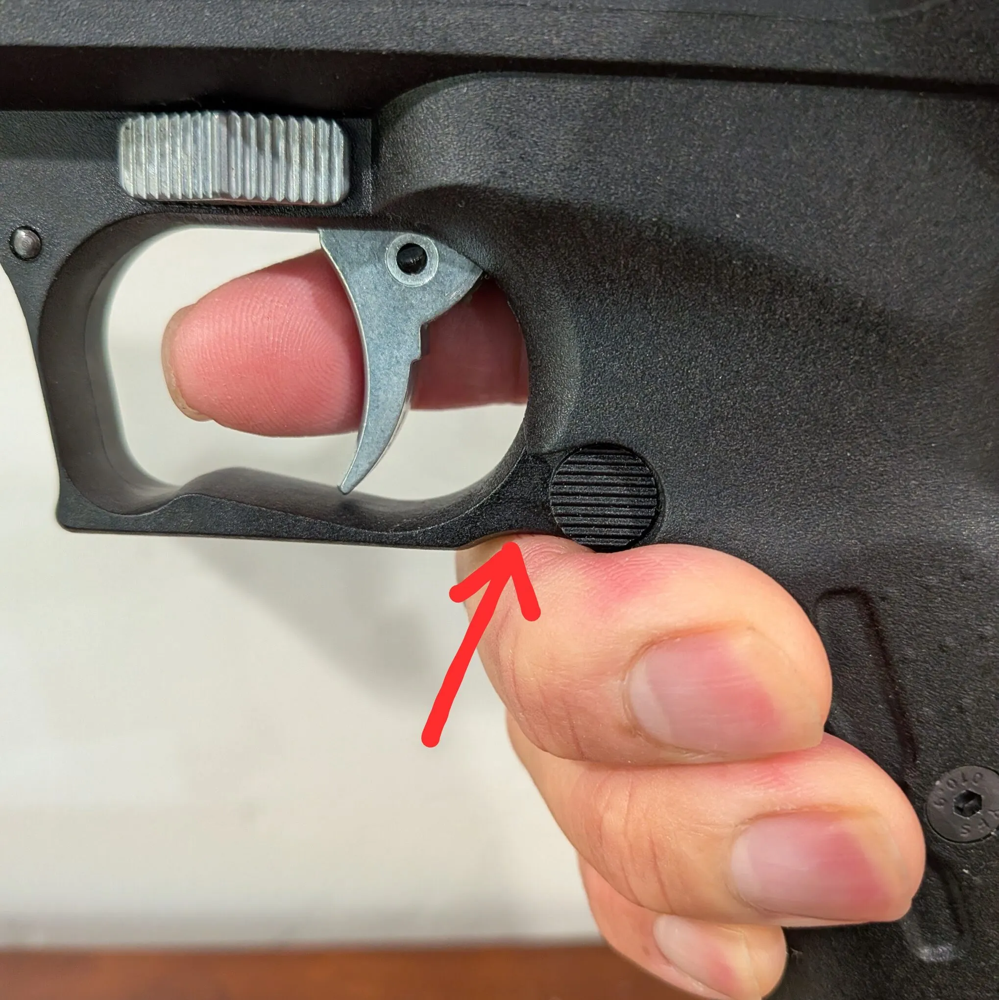 HW40 held in the hand, with a red arrow pointing to the upward curve beneath the rear of the trigger guard above the middle finger