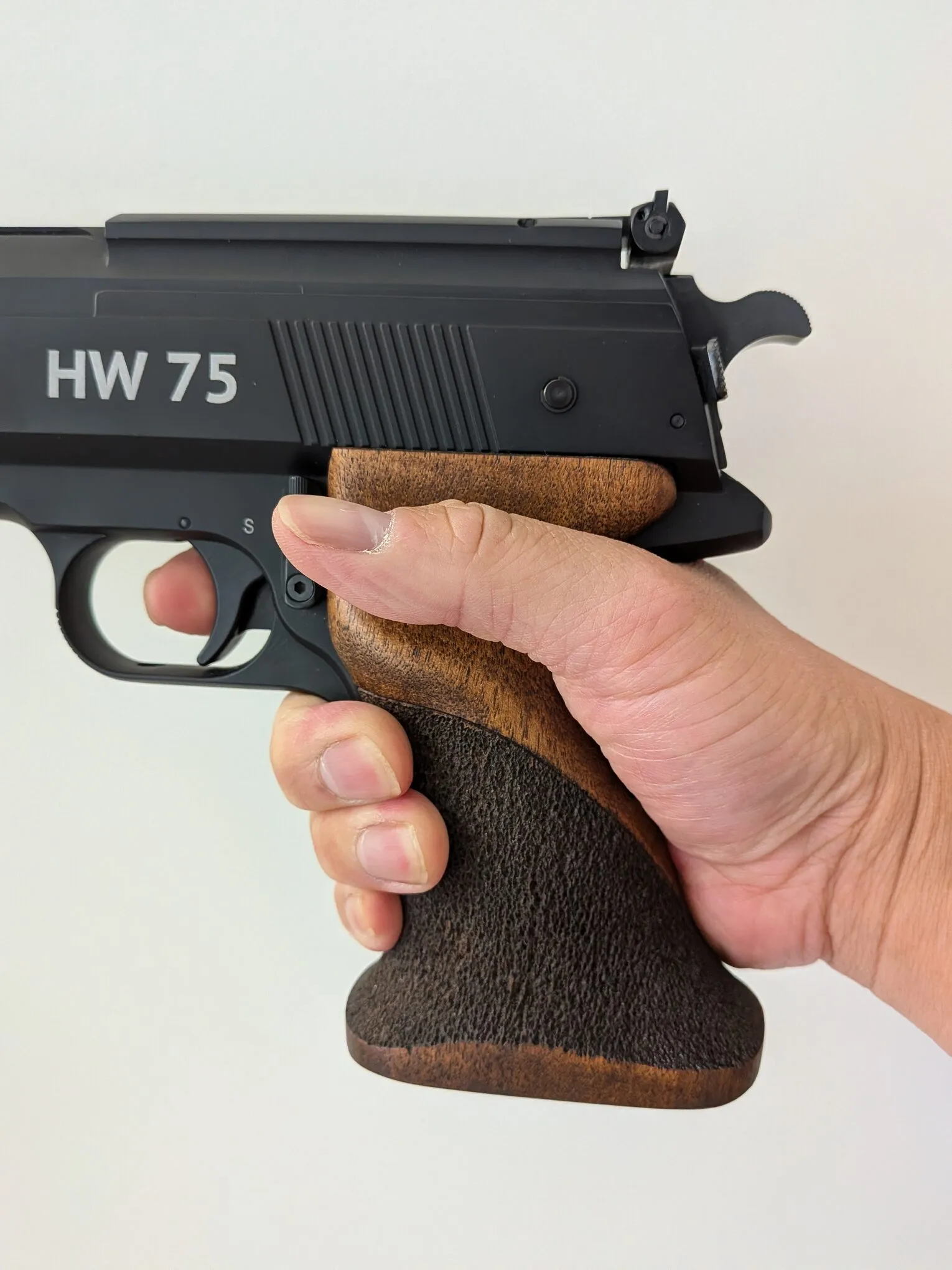 Side view of the HW75 grip in the hand, showing the thumb rest and the three fingers supporting the pistol