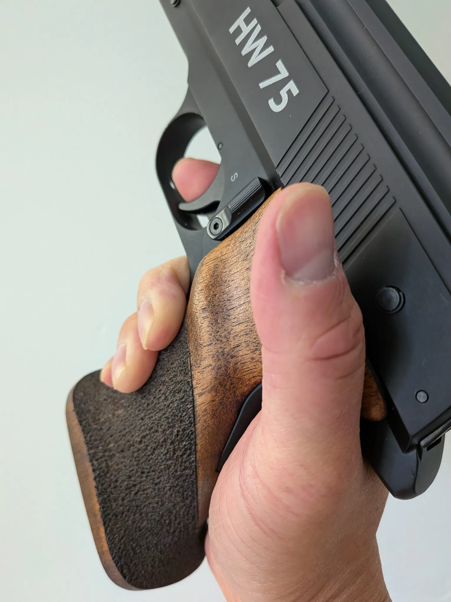 Close-up of the thumb resting higher alongside the HW75 frame and walnut grip