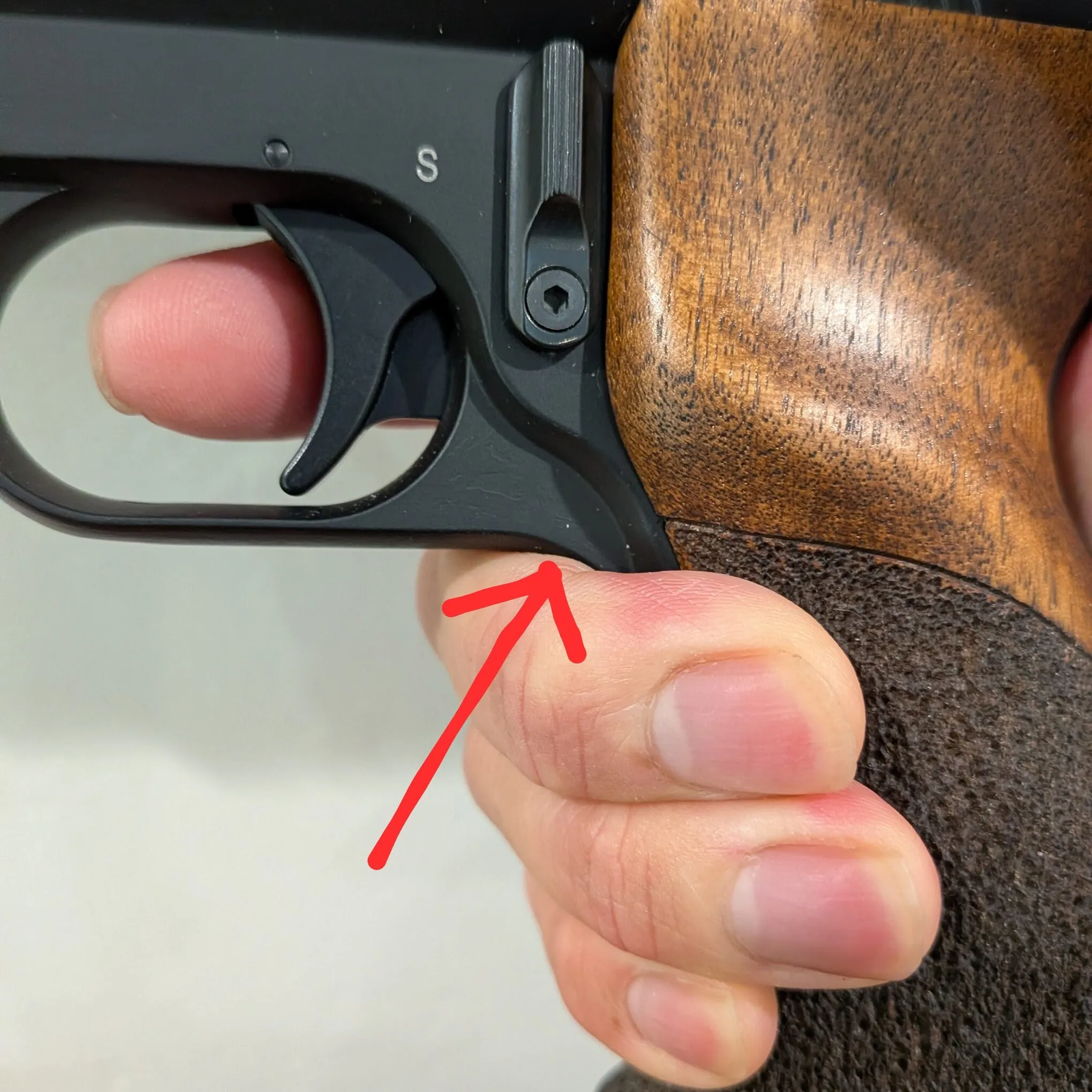 HW75 held in the hand, with a red arrow pointing to the flat underside of the trigger guard resting on the middle finger